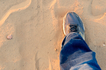 Fototapeta na wymiar Top down view of man extending a foot with a worn sneaker jeans on dusty sand showing travel and trekking during evening as sunlight bounces off it