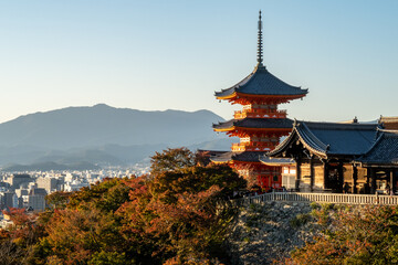 Red traditional pagoda of Buddhist Temple Kiyomizu-dera in Kyoto, with Kyoto landscape in the background, golden hour view, Japan, autumn