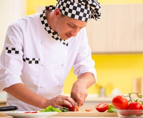 Young professional cook preparing salad at kitchen