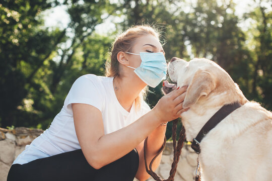 Lovely Blonde Woman With Medical Mask On Face Playing With Her Dog Outside During The Lockdown