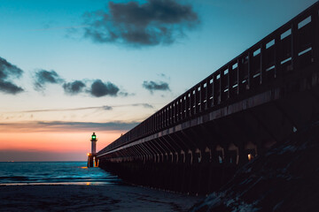Pier at sunset leading to a small lighthouse on a french beach