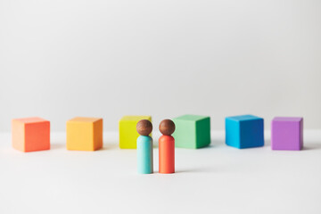 Wooden figures concept. Couple standing in front of wooden blocks in colours of the gay pride rainbow flag. Couple of dark skin colour. 