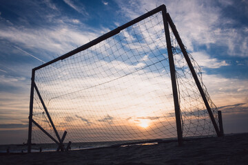 Silhouette of an empty soccer goal on a beach with a beautiful sunset in the background