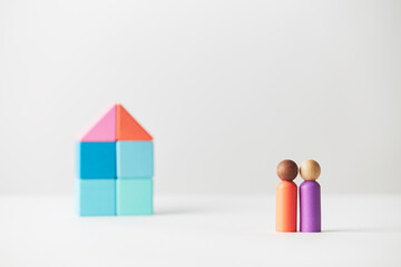 Wooden figurines concept. Two wooden figures people standing in front of a large multi generations block house, mixed race skin colour, four adults. Realty market.