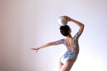 Girl gymnast doing exercise with silver ball (back view)