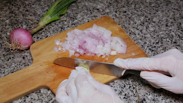 Chef's hands chopping onion and garlic seen from above