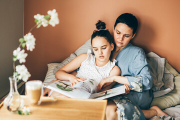 Mother and daughter enjoy in bed at home. Morning awakening. mother and daughter reading a book together in bed in the morning