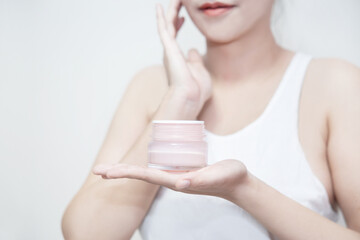  woman hold a moisturizer cream in her hand and applying the cream on her face