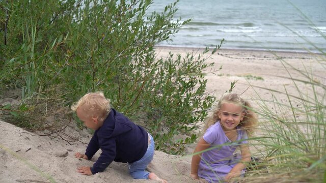 Adorable children fighting on dune sand. Brother and sister have fun at beach