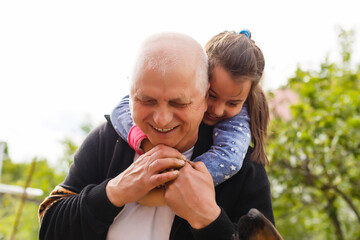 Portrait of small girl with senior grandfather in the backyard garden, standing.