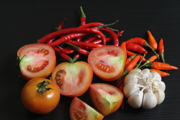 A few of portion cut tomatoes, garlic, and red chilies on black table.