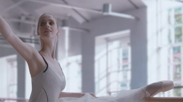 Caucasian female ballerina practicing moves in a bright modern bright large dance studio, daytime shot.