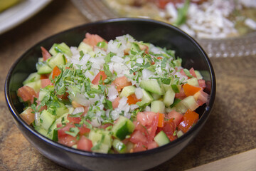 Fresh Israeli vegetables salad, containing cucumber, tomato white onion and parsley, served in a dark bowl 