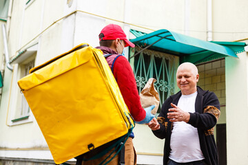 Courier in protective mask and medical gloves delivers takeaway food. Delivery service under quarantine, disease outbreak, coronavirus covid-19 pandemic conditions.