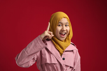 Fototapeta premium Asian muslim young teenage girl wearing hijab smiling for having good idea with finger pointing up