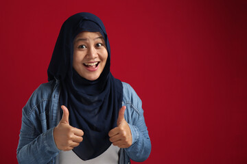 Portrait of young Asian muslim lady wearing hijab shows thumbs up gesture, smiling happy face, approved OK sign