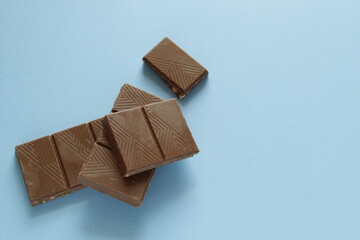 Milk chocolate pieces isolated on blue background from top view. Close up a chocolate bar isolated on blue background.