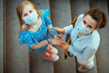 stylish mother and daughter disinfecting hands with sanitiser