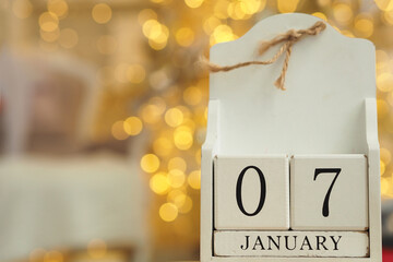 White wooden calendar with cubes and date January 07 and lights bokeh from a garland in the background. Orthodox Christmas date. Copy space..