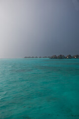 Maldivian water villas and jetty seen from turquoise ocean in the rain