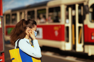 woman wearing medical mask at tram stop outdoors on city street