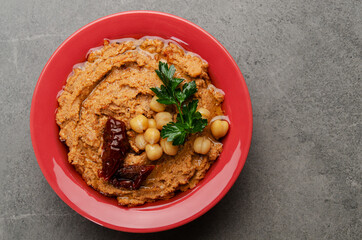 Flat lay view at hummus topped with chickpeas, sun dried tomatoes and green coriander leaves on stone table