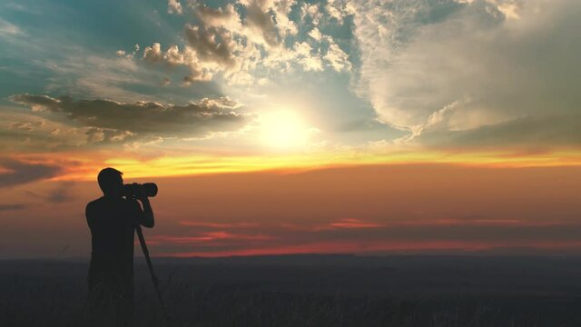 The man use the camera with tripod against the beautiful sunset background