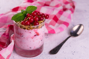A glass of yogurt with granola and red currant berries on a white background.
