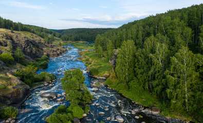 Fototapeta na wymiar Ural Mountains. Rocks and rocky rifts on a mountain river in summer. View from the drone on valley and the river Iset with rocky banks.
