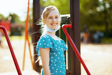smiling modern child with mask on playground outdoors in city