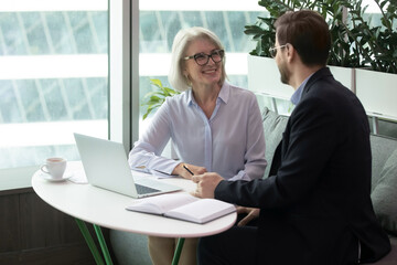 Female boss discusses work issues with subordinate middle aged man, sitting at the table....