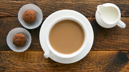 Coffee cup with cream and chocolate truffles on wooden table, top view