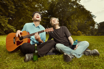 Two men on city park summer meadow enjoying day with guitar