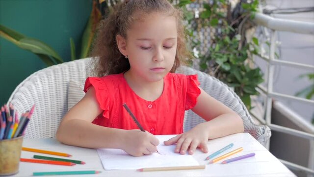Happy Little Girl or Cute primary child school child of 7-8 years old at home relaxing sits in house and paints on paper use colour pencils. Child draws,focused children elementary education concept.