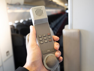 Male cabin crew holding interphone in aircraft cabin. 