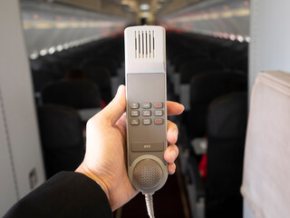 Male cabin crew holding interphone in aircraft cabin. 
