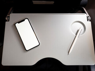 Tray table in aircraft economy class. small working space when travel. Small space for having food. Air sickness bag in seat pocket. Table with phone and pen in aircraft.