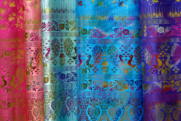 Lengths of colorful silk fabric with a peacock and floral motif for sale at an open-air market in Xishuangbanna, Yunnan Province, China