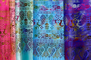 Lengths of colorful silk fabric with a peacock and floral motif for sale at an open-air market in Xishuangbanna, Yunnan Province, China