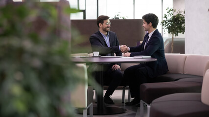 Two smiling business men shaking hands after successful meeting. Leader businessman handshaking of new worker after well done job interview or happy partners making deal with handshake