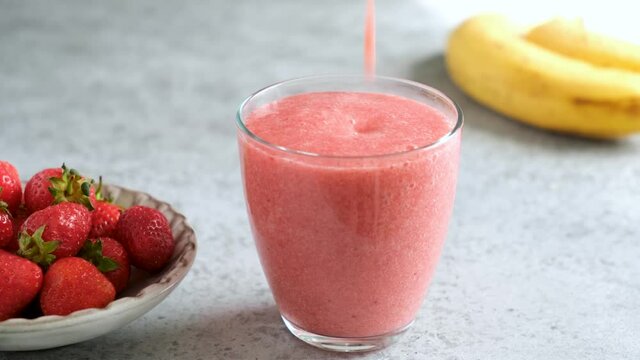 Pouring strawberry smoothie in drinking glass. Raw vegan strawberry smoothie