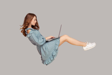 Hovering in air. Pretty girl ruffle dress levitating, typing keyboard using laptop for work online,...