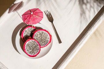 Dragon fruit, pitaya on a white wooden tray on the sand of tropical beach under a palm tree. Exotic...