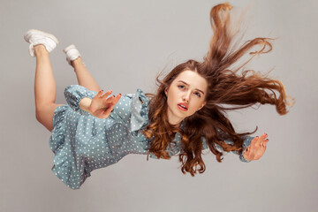 Beautiful girl levitating in mid-air, falling down and her hair messed up soaring from wind, model...