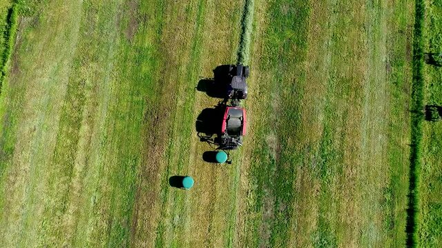 Schwarzer Treker mit einer roten Stroh Festkammerpresse bei der Strohernte auf einem gem&auml;hten Feld