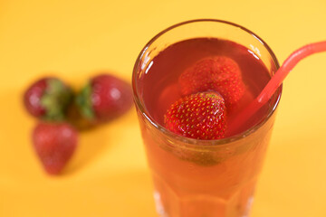 Fresh summer cocktail with strawberries and ice cubes on a yellow background, close-up.