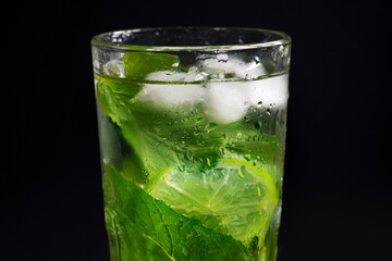 Mojito refreshing cocktail with mint leaves, lime and ice on a black background.