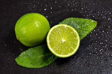 Fresh lime with mint leaves and drops of water on a dark background. Tropical citrus fruits. Top view.