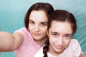 Two beautiful sisters smiling take a selfie on their smartphone on a blue background.