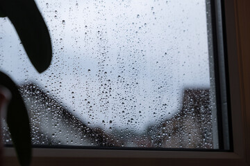 Dunkles Regenwetter mit grauen Himmel und vielen Regentropfen an der Fensterscheibe.